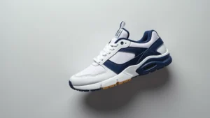 Professional overhead shot of white and navy Air Tech Challenge 2 sneaker on minimalist gray background, showing detailed upper construction and side profile silhouette, photorealistic product photography