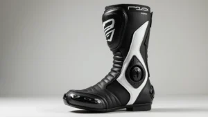 Professional motorcycle racing boot in black and white leather, showing internal ankle padding and protective shin plate, photographed at eye level against neutral background