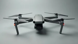 High-quality overhead shot of a modern carbon fiber drone with folded arms, metallic gray finish, professional gimbal visible, photographed against neutral gray background with studio lighting